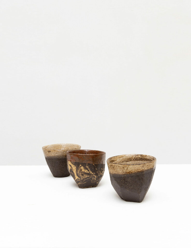 Trois tasses en céramique artisanales sur table blanche.
